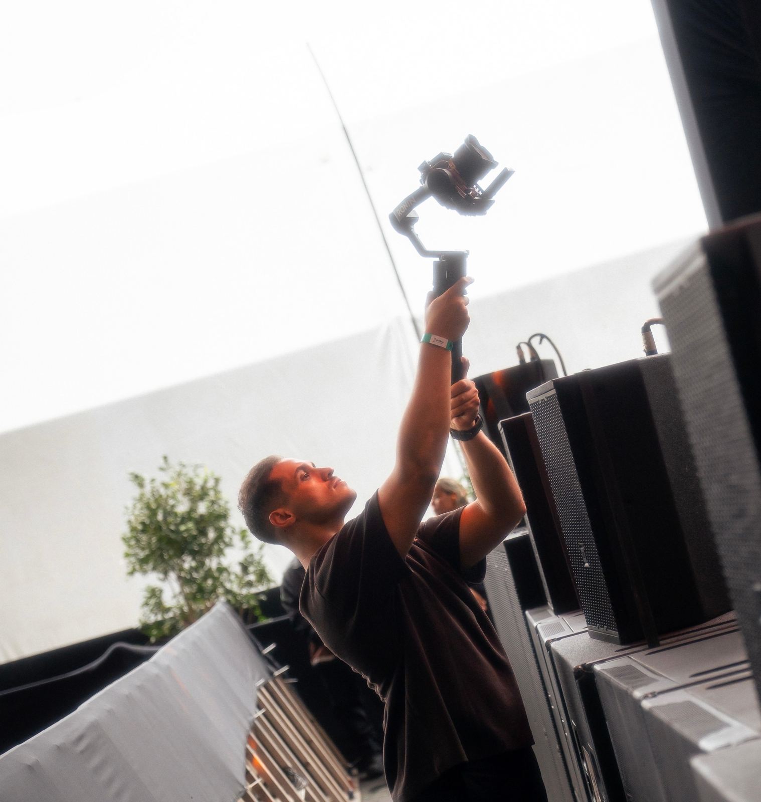 Juan Ramirez com os braços erguidos segurando o gimbal ao lado das caixas de som